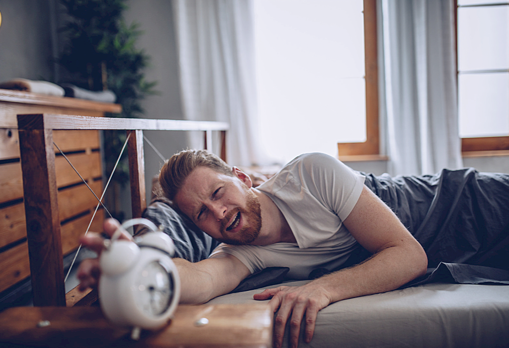 Sleepy man reaching for alarm clock